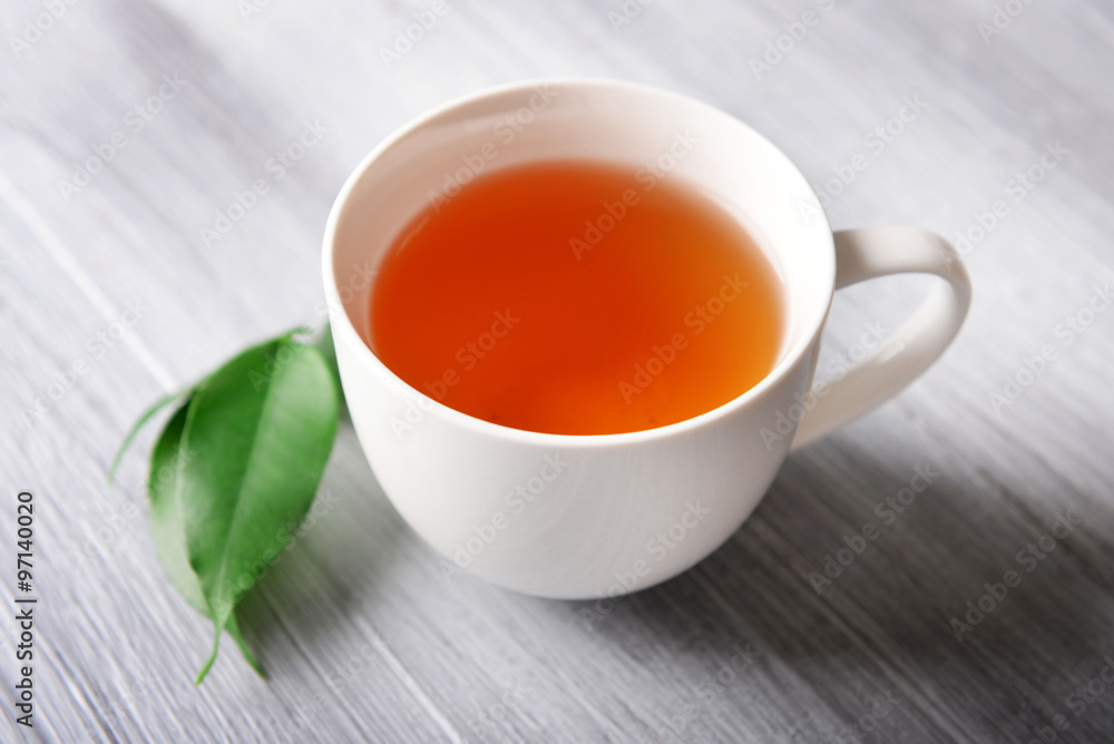 Ceramic cup of tea with green leaves on light wooden background Ceramic cup of tea with green leaves on light wooden background