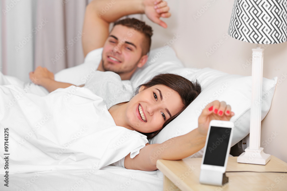 Fototapeta premium Happy couple waking up with mobile alarm clock