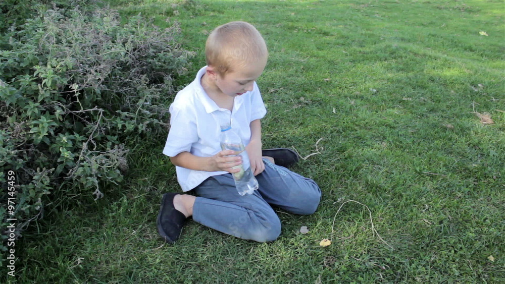 boy sitting on the grass/boy sitting on the grass and holds water bottle boy sitting on the grass/boy sitting on the grass and holds water bottle
