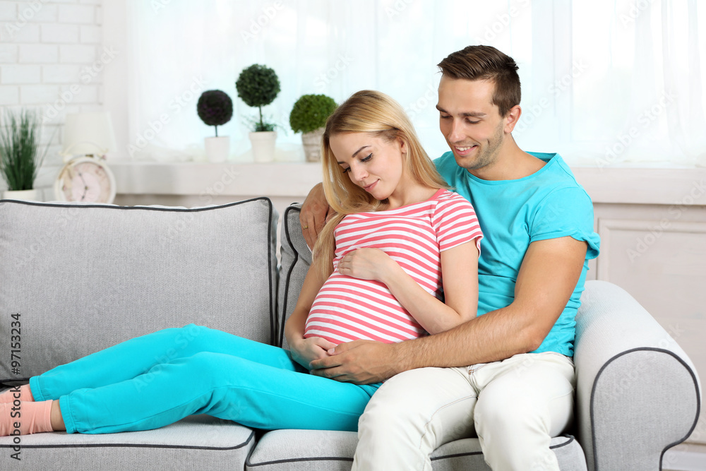 Young pregnant woman with husband on sofa in room