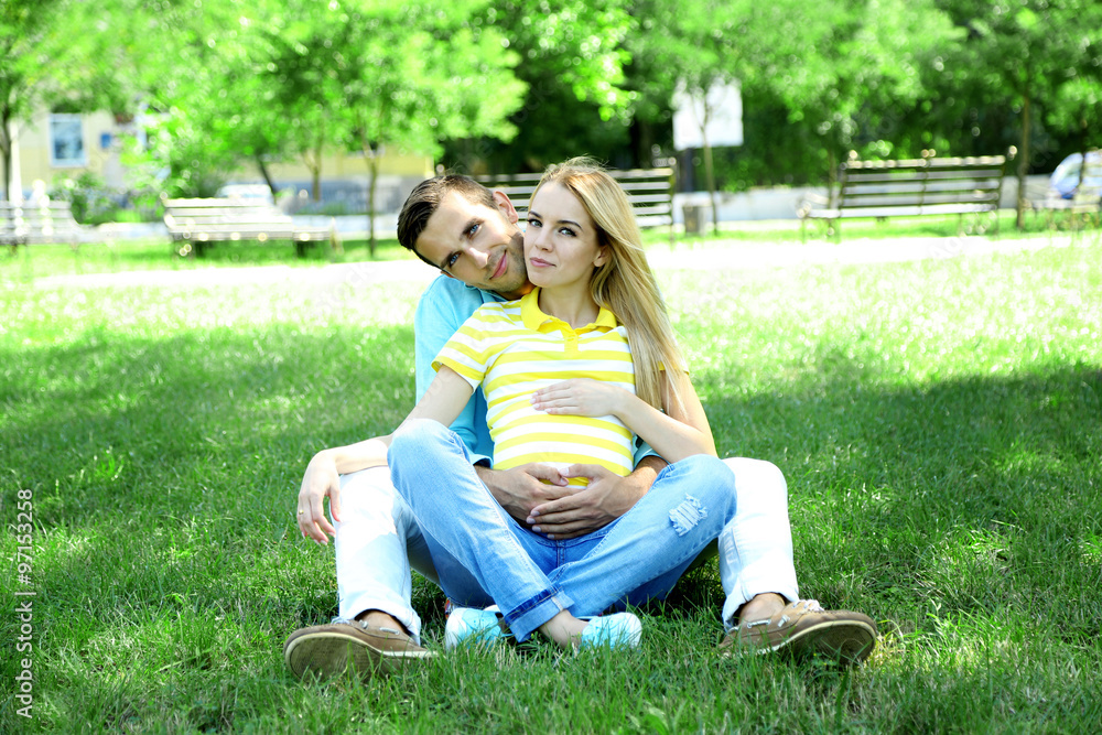 Young pregnant woman with husband sitting on green grass in park Young pregnant woman with husband sitting on green grass in park