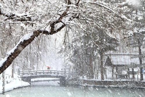 雪のふる街の橋を渡る赤い傘をさすを女性