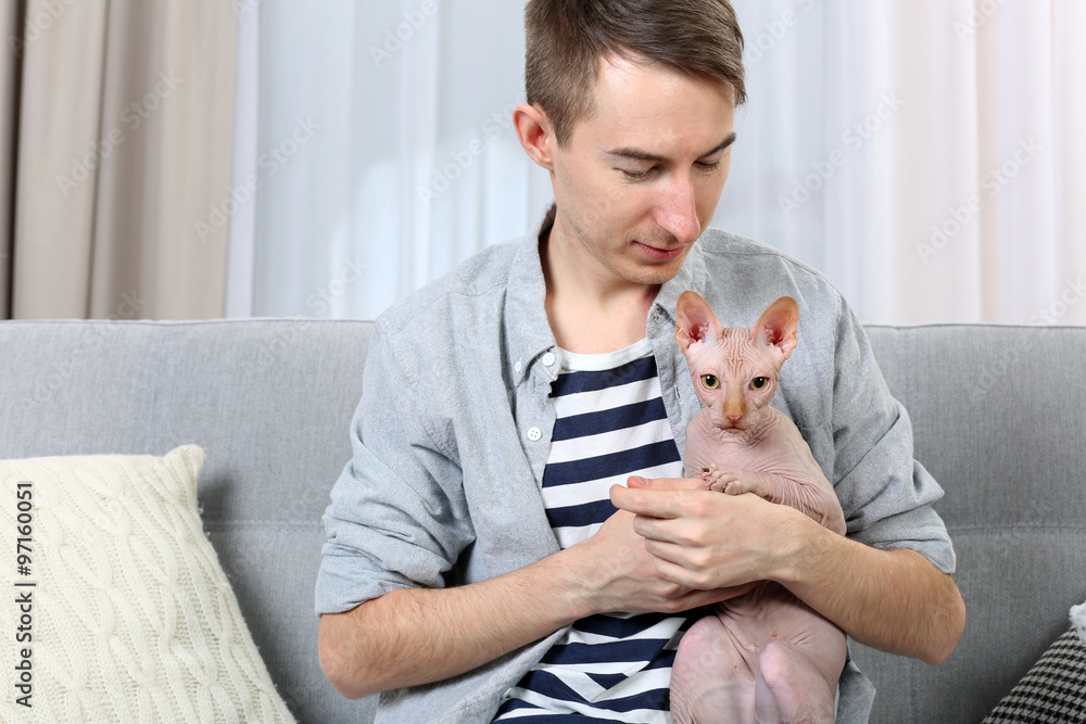 Young handsome man holding a cat on light room background Young handsome man holding a cat on light room background