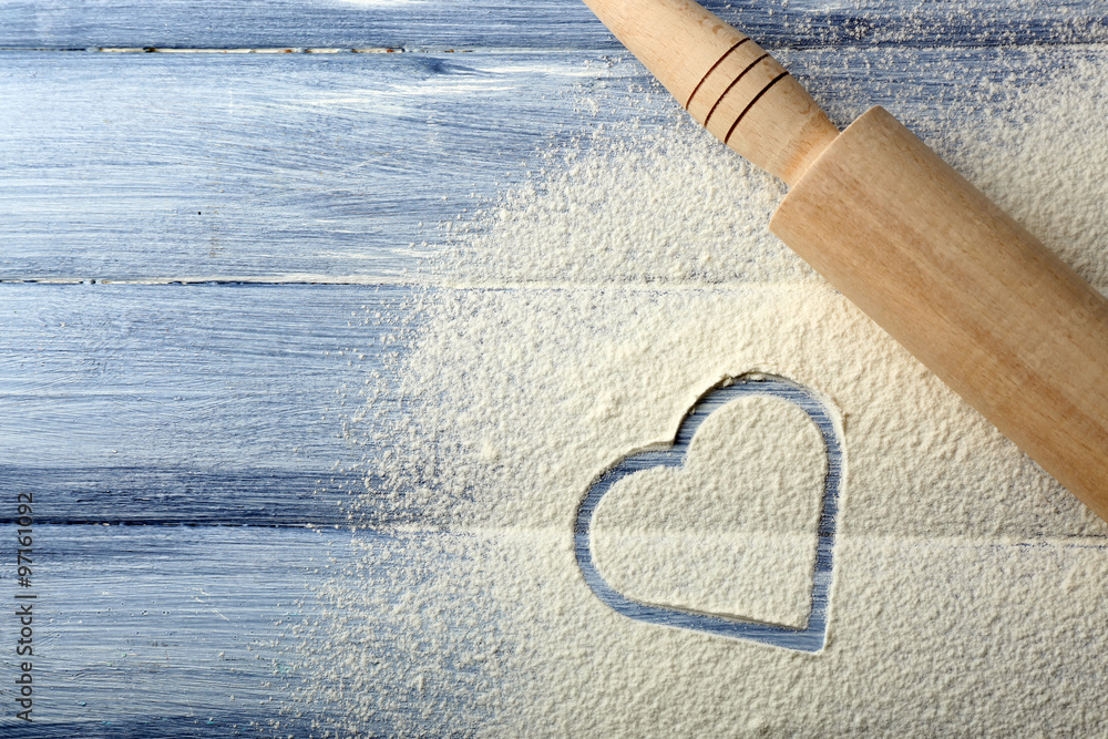 Heart of flour and rolling pin on color wooden background