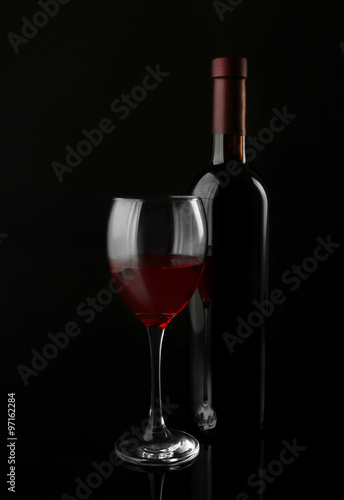 Red wine glass and bottle on black background, close up