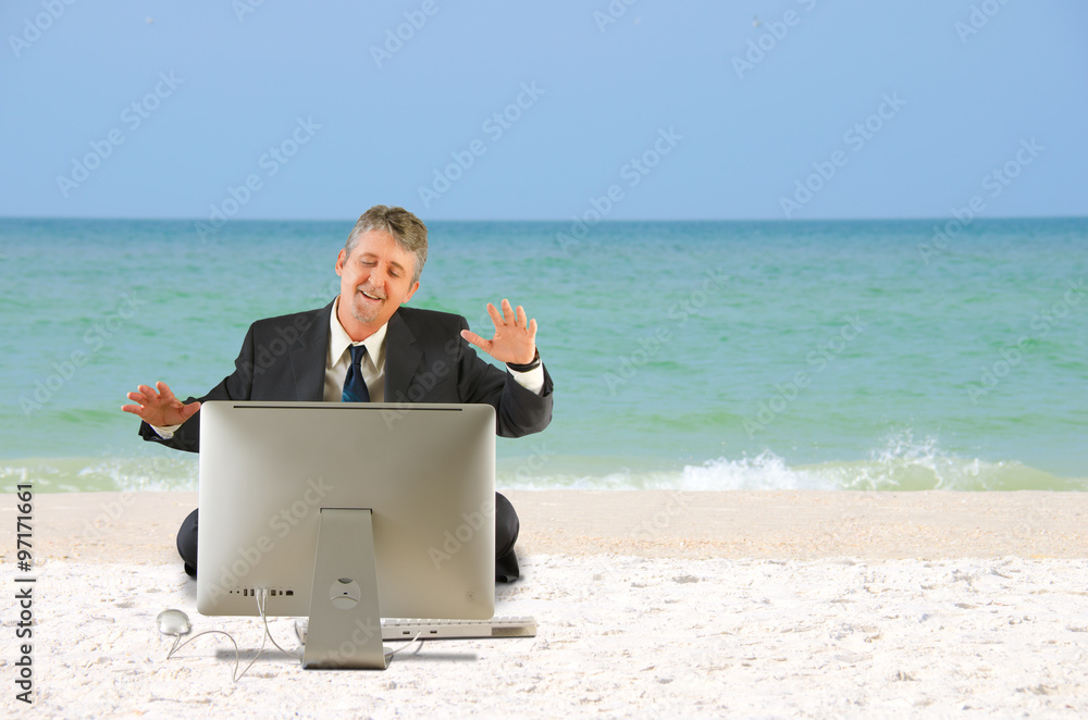 A business man in a suit is sitting on the beach with a big computer in front of him and he has a very happy look on his face