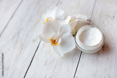 pot of  face cream and beautiful white orchid flowers on white  wooden table