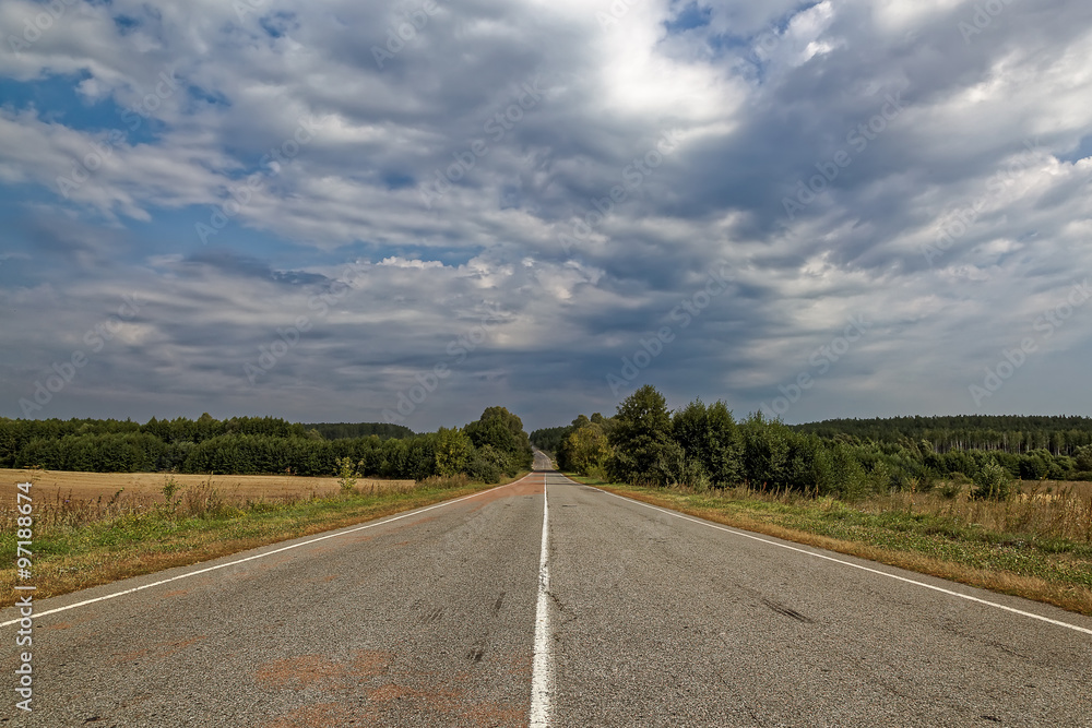 Fototapeta premium Asphalted road against the blue sky with clouds.