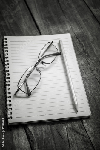 Black and white photo of notebook, pen and glasses on the table