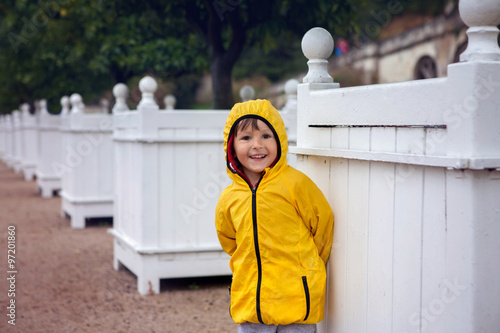 Cute boy in blooming garden, summertime on rainy day