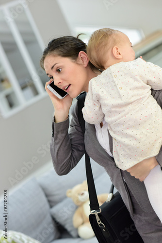 Busy businesswoman talking on phone and holding baby in arms photo