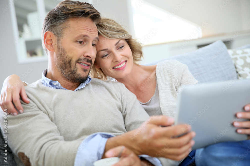 Middle-aged couple relaxing in sofa and using tablet