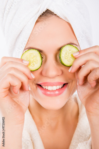 Beautiful woman holding cucumber slices on the face. White backg