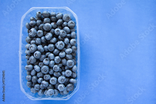 plastic box full of blueberries on blue background