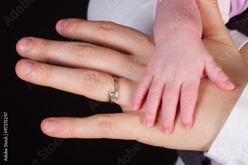Mother holding baby hand, black background
