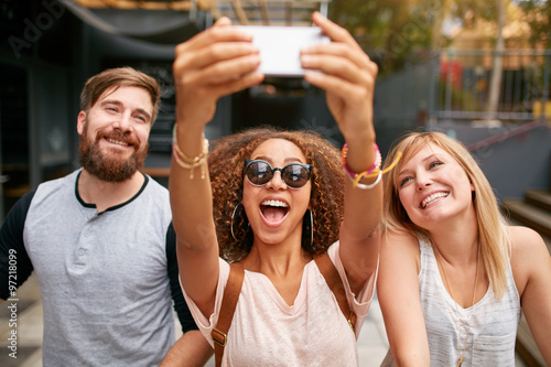 Group of smiling friends taking selfie with smart phone