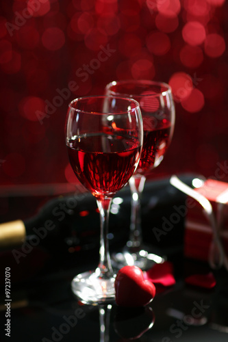 Setting of glasses with wine, bottle and a gift in the box, on red blurred background