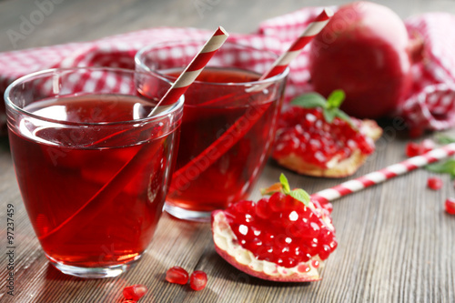 Two glasses of tasty juice and garnet fruit, on wooden background