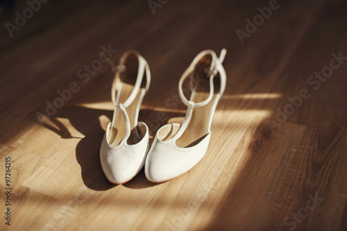 Elegant stylish white leather bride shoes on wooden floor closeu