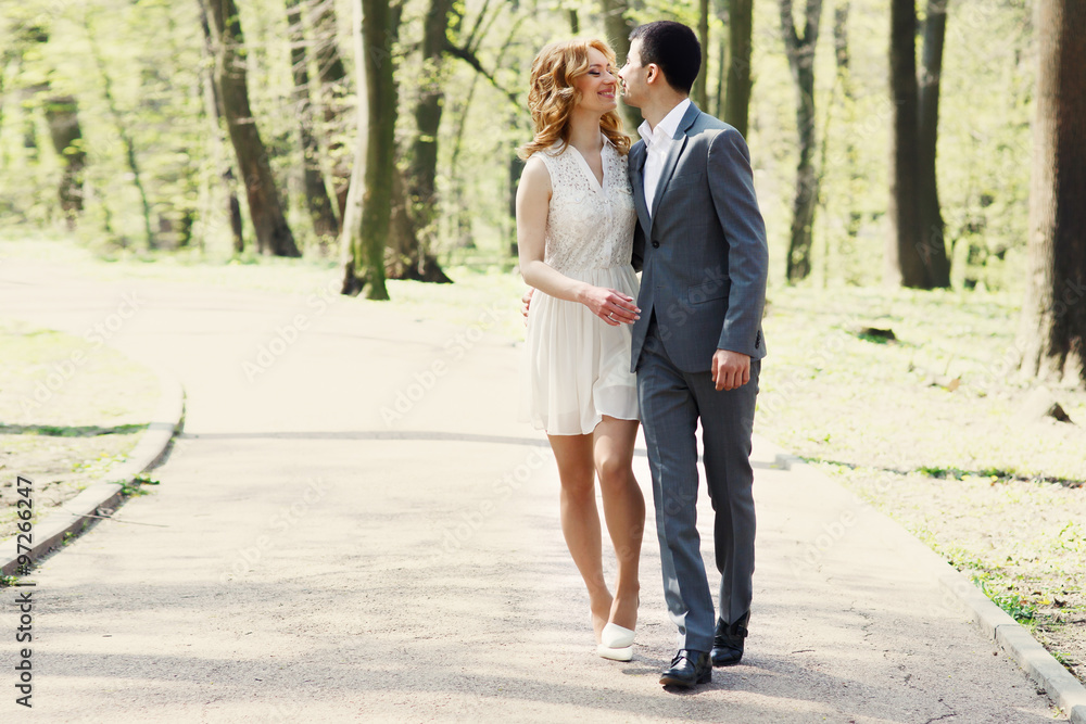 Fototapeta premium happy wedding couple, elegant bride and handsome groom walking in sunlit park