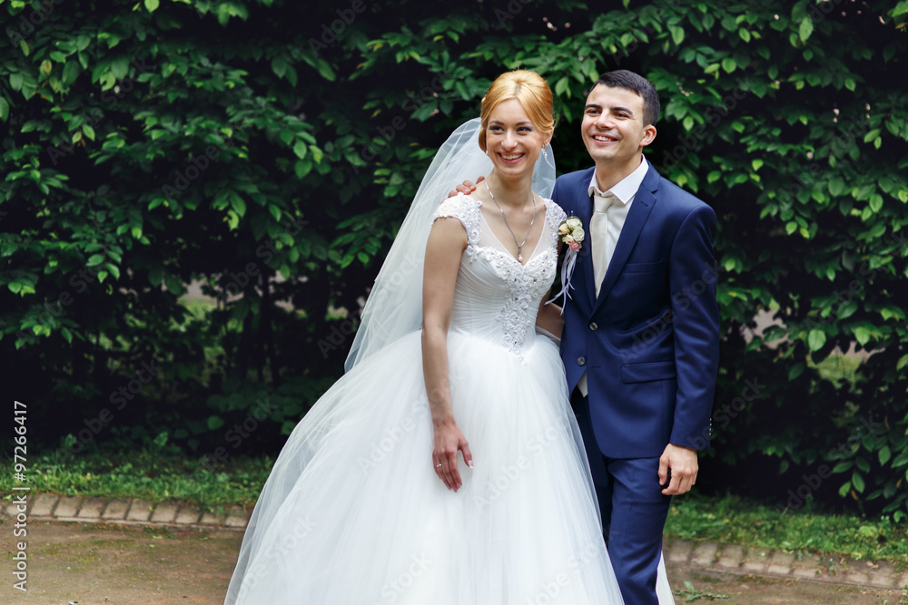 Stylish blonde bride in vintage dress and handsome happy groom holding hands and smiling outdoors