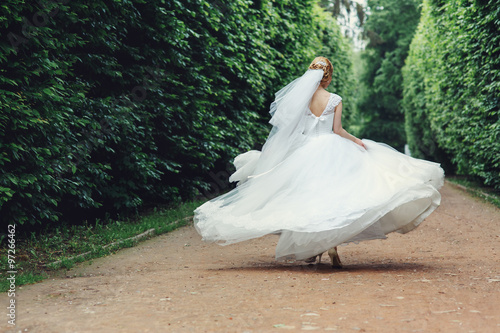 Gorgeous stylish blonde bride in vintage white dress walking in the park