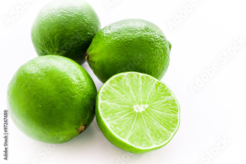 Close up photo of one cut-in-half slice of lime, with three whole lime behind. The background is isolated.