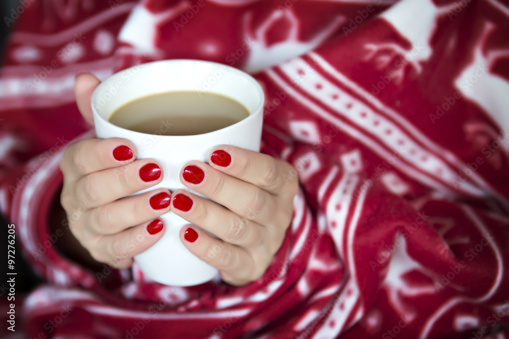 A woman wrapped in a blanket with a cup of hot drink