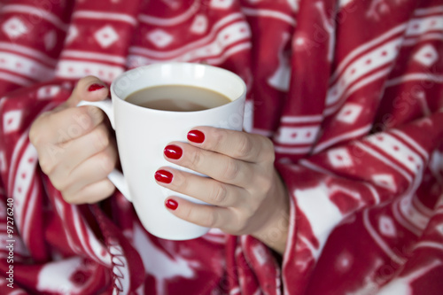 A woman wrapped in a blanket with a cup of hot drink