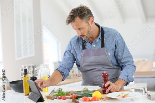 Man in kitchen cooking dish and using digital tablet