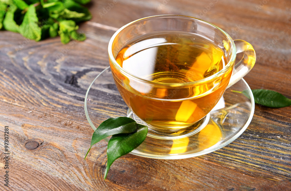 Glass cup of tea with green leaves on wooden background Glass cup of tea with green leaves on wooden background