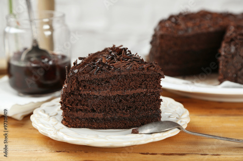 Sliced chocolate cake on wooden table, on light background