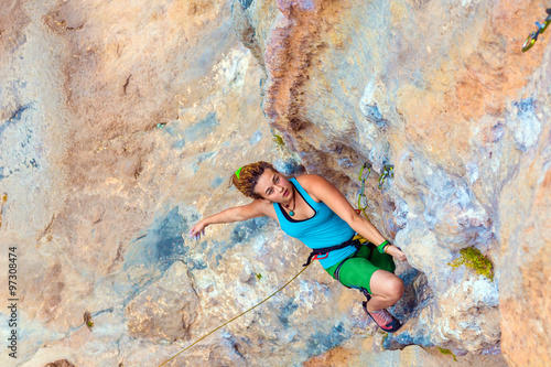 Young Cute Climber on orange blue vertical wall Female Athlete climbing natural rock keeping hold and hanging over deep abyss