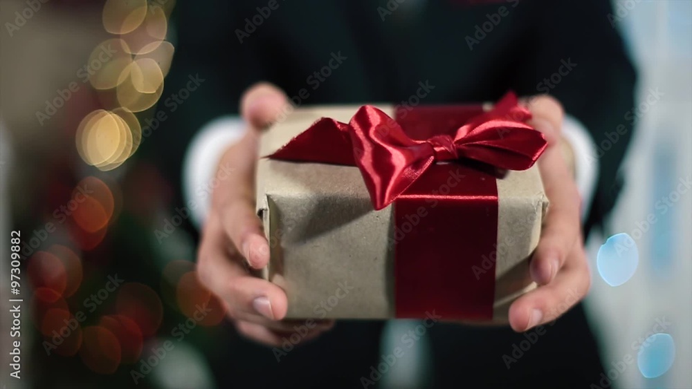 A man In a black suit gives a gift to the viewer, the light of the Christmas tree A man In a black suit gives a gift to the viewer, the light of the Christmas tree