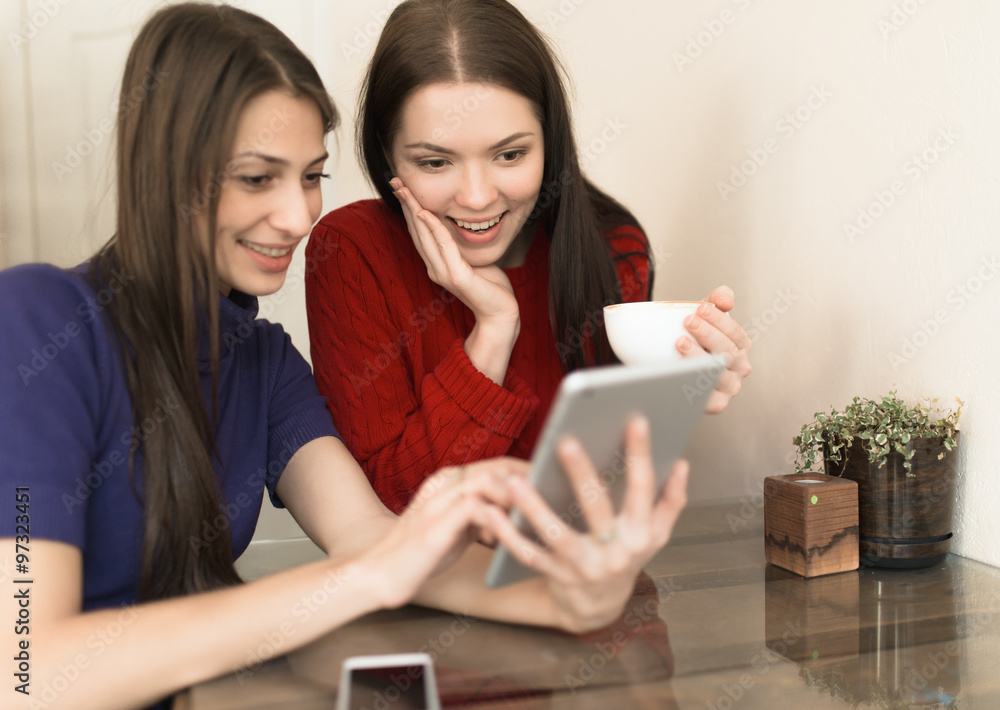 Two girlfriends using tablet in light coffee shop