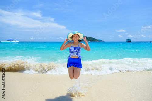 Tourist woman in a blue white striped swimsuit jumping with happy on the beautiful beach sea and sky during summer at Koh Miang Island, Mu Ko Similan National Park, Phang Nga, Thailand