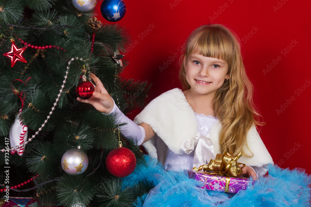 Beautiful baby girl in a dress  sitting  near the Christmas tree in New Year's Eve smiling and looking for a gift