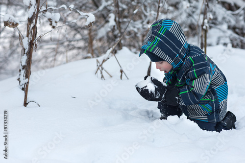 Boy eating snow in the winter woods.