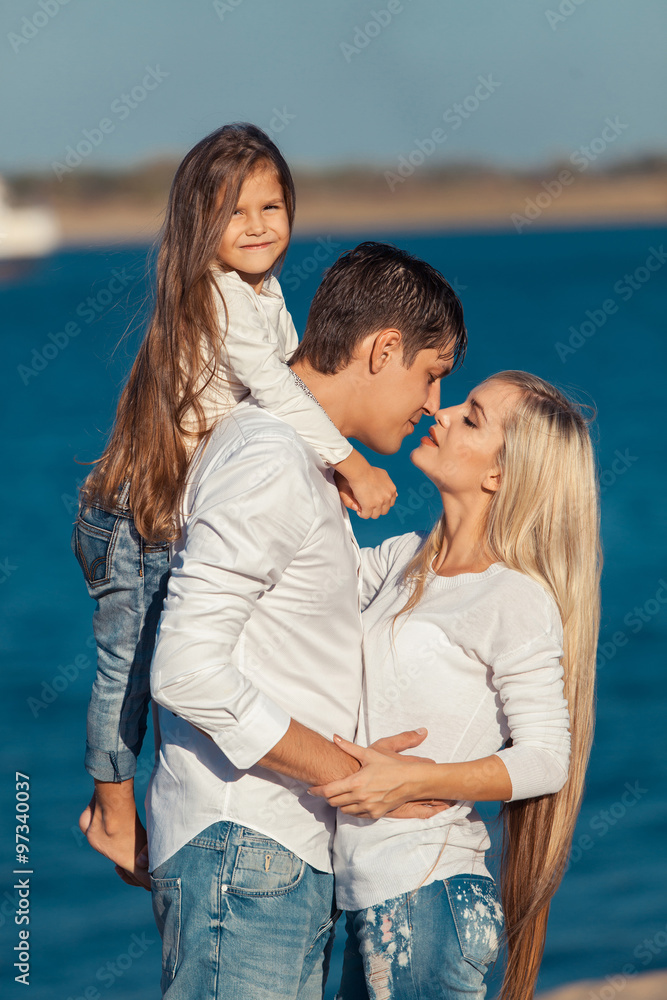 Young family in blue jeans hugging on the background of water Young family in blue jeans hugging on the background of water