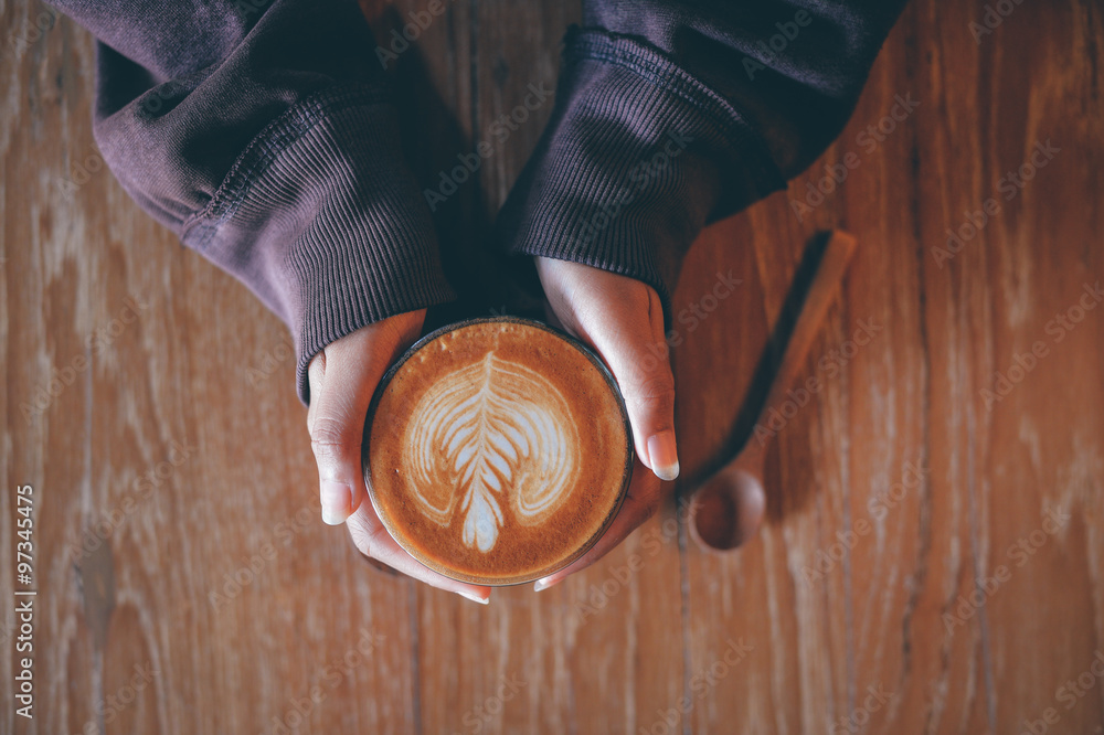 Woman hand hold cup of coffee latte on the wood texture in vintage color tone Woman hand hold cup of coffee latte on the wood texture in vintage color tone