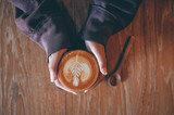 Woman hand hold cup of coffee latte on the wood texture   in vintage color tone