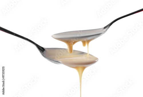 Condensed milk pouring from spoons  isolated on white