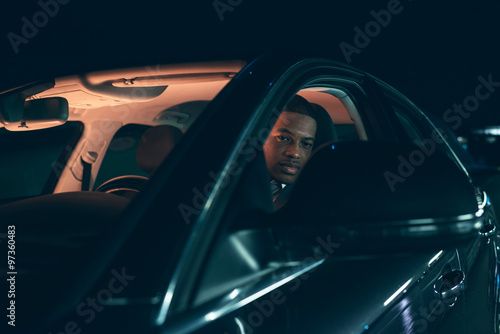 Young hispanic man looking in side mirror of car at night.