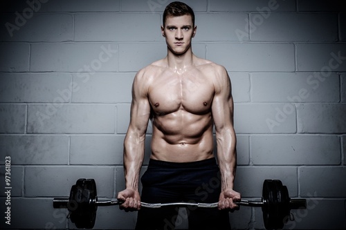 Athletic man doing exercises with barbell in The Gym's Studio