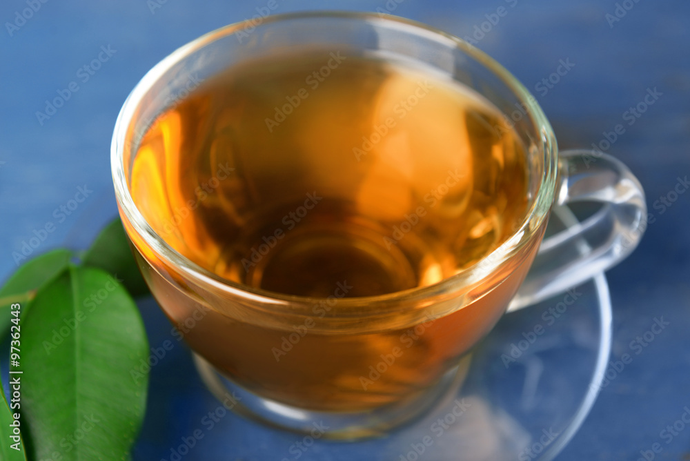 Glass cup of tea with green leaves on blue wooden background Glass cup of tea with green leaves on blue wooden background