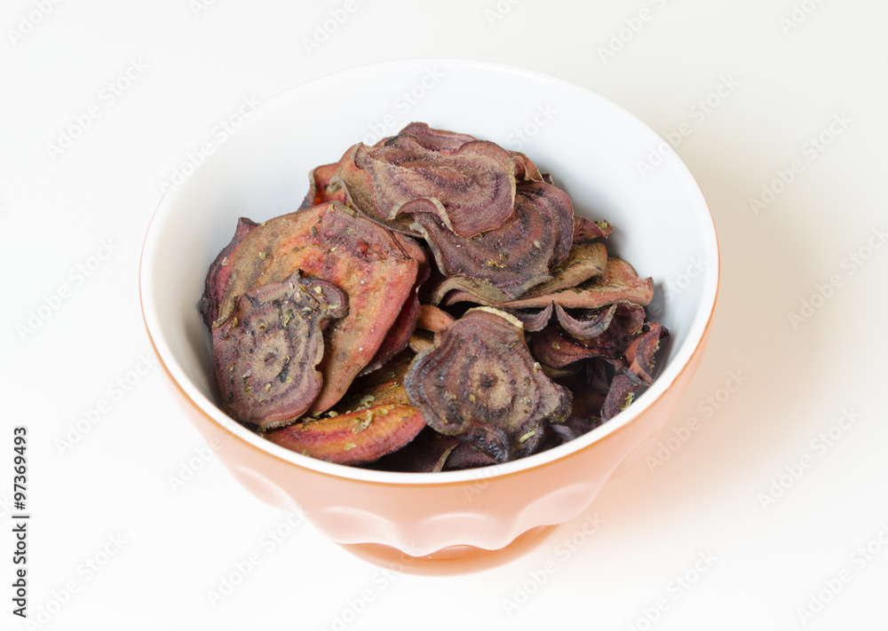 Thin round beetroot chips baked in the oven with oregano and salt and ripe beet roots in a bowl isolated on white background.Healthy,vegetarian,vegan,crispy snack appetiser for diet and clean eating Thin round beetroot chips baked in the oven with oregano and salt and ripe beet roots in a bowl isolated on white background.Healthy,vegetarian,vegan,crispy snack appetiser for diet and clean eating