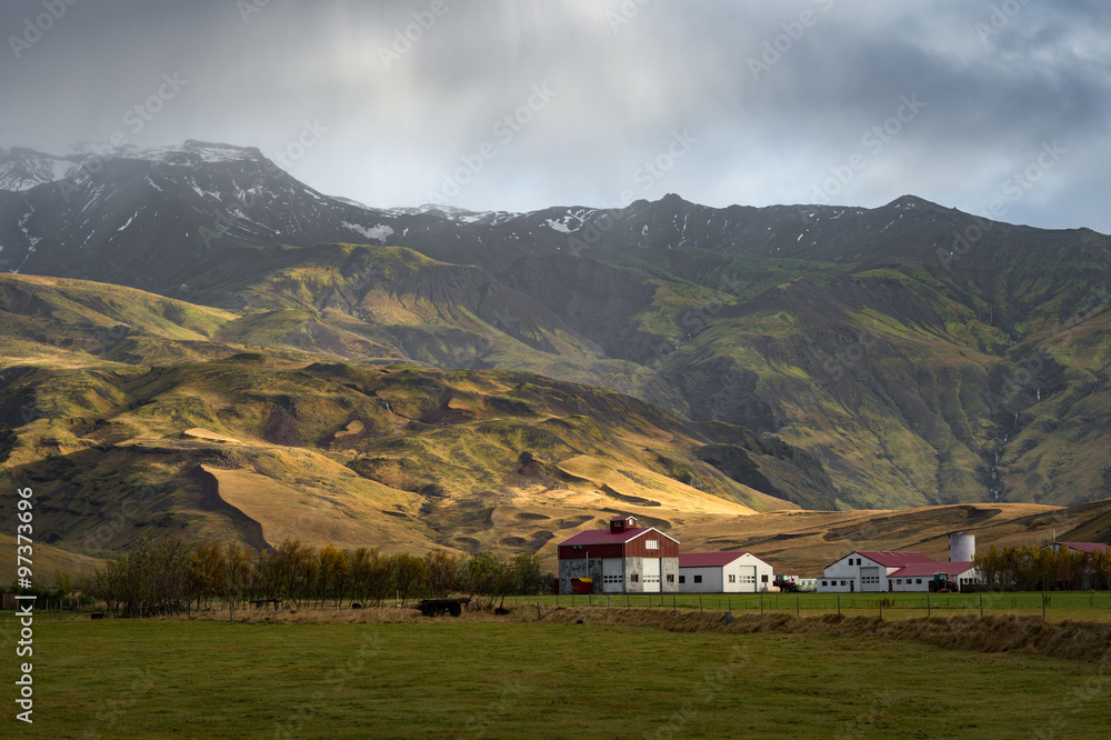 White barn with red roof in green filed surround by mountain range in Autumn season