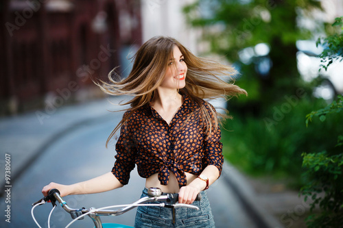 Pretty girl is standing at the street on blouse and shorts with bicycle