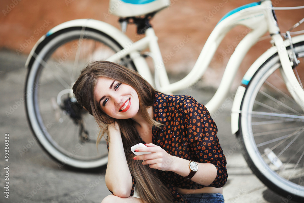Obraz premium Smiling young girl with long straight hair is sitting on tiled pavement in old city