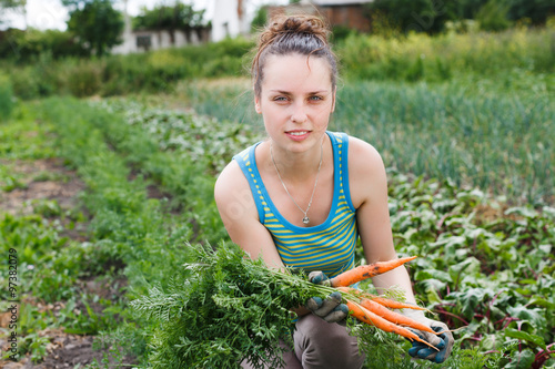 Young brunet woman is holding bunch of fresh organic carrots in her hand and looking at camera